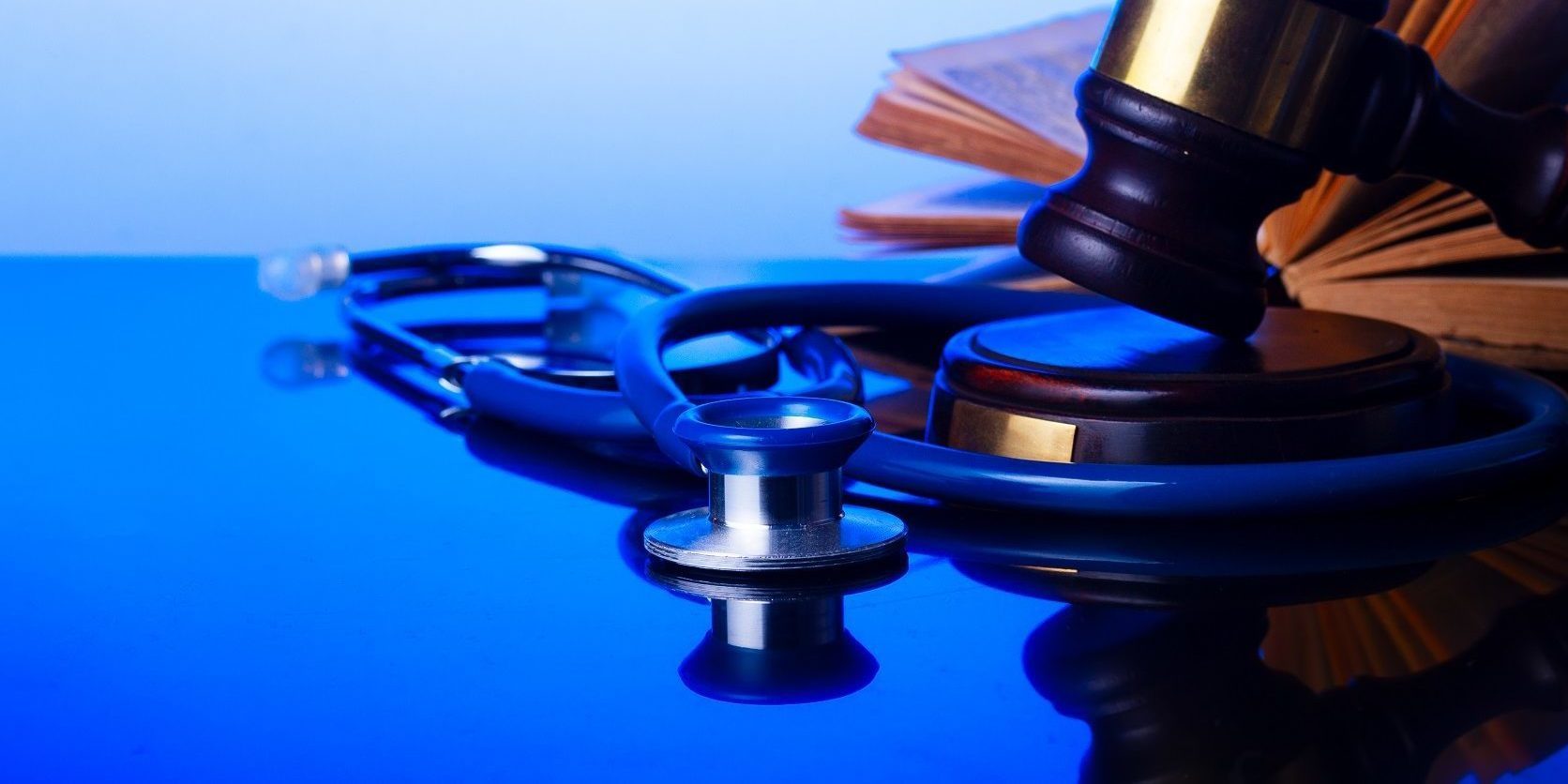 Wooden law gavel with stethoscope and open book - medical law and justice concept
